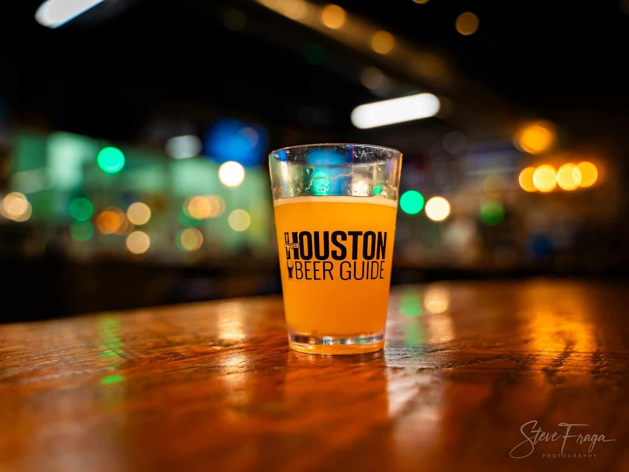 A pint glass with the Houston Beer Guide logo on a bar top